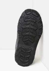Czarna gumowa podeszwa z wielokierunkowym wzorem bieżnika i teksturowaną powierzchnią. Zawiera odcisk logo i wypukłe akcenty dla lepszej przyczepności.