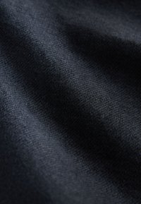 Close-up van donkergrijs geweven stof met zichtbare textuur en zachte plooien die schaduwen en highlights creëren.