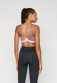 Μωβ αθλητικό σουτιέν με ρυθμιζόμενες τιράντες και κλείσιμο με γάντζο, συνδυασμένο με μαύρο κολάν υψηλής μέσης. Λείο υλικό, μινιμαλιστικός σχεδιασμός.