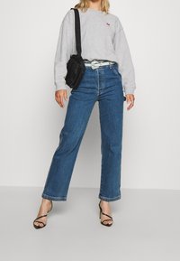 Gray sweatshirt with a small red logo, blue wide-leg jeans, black crossbody bag, and black strappy high-heeled sandals.