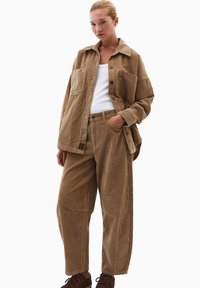 Set di camicia e pantaloni oversize in corduroy marrone, caratterizzato da una vestibilità rilassata, tessuto testurizzato, grandi tasche frontali e design con bottoni.