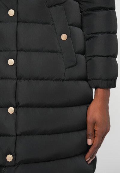 Black padded jacket featuring horizontal quilted sections, gold-tone snap buttons, and a side pocket detail. Smooth texture.