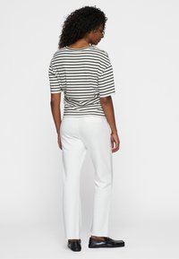 Top a righe bianche e nere con maniche corte e una vestibilità ampia, abbinato a pantaloni bianchi e scarpe nere, visto da dietro.