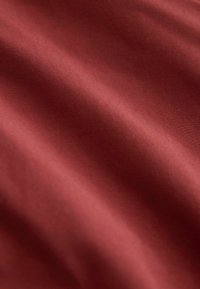 Tissu bordeaux à texture lisse, présentant un éclat subtil et un léger drapé. La surface affiche une couleur uniforme et homogène.