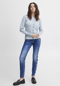 Gai zils garie svārki ar pogām, kombinēti ar ziliem džinsiem ar izsistu ceļgalu un melnām loaferām.