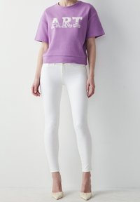 Lila cropped sweatshirt med "ART" tryck, kombinerad med vita skinny jeans och off-white klackar. Slät tyg och figurnära design.
