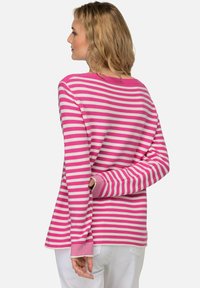 Felpa a maniche lunghe a righe rosa e bianca, con vestibilità comoda, scollo rotondo e polsini a coste. Indossata con pantaloni bianchi.