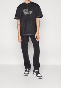 Svart mesh oversized t-shirt med "ACID HOUSE" tryckt i silver. Kombinerad med svarta jeans och svartvita sneakers. Enkel, sportig look.