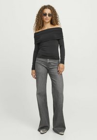 Crna off-shoulder bluza s dugim rukavima i sakupljenim materijalom, u kombinaciji s rasirenim sivim trapericama i srebrnim cipelama s špicastim vrhom.