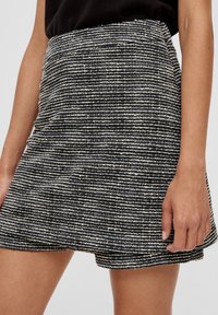 Sukně s černobílými pruhy vyrobená z texturované látky, s oblým lemem a přiléhavým střihem. Žádné viditelné kovové prvky nebo ozdoby.