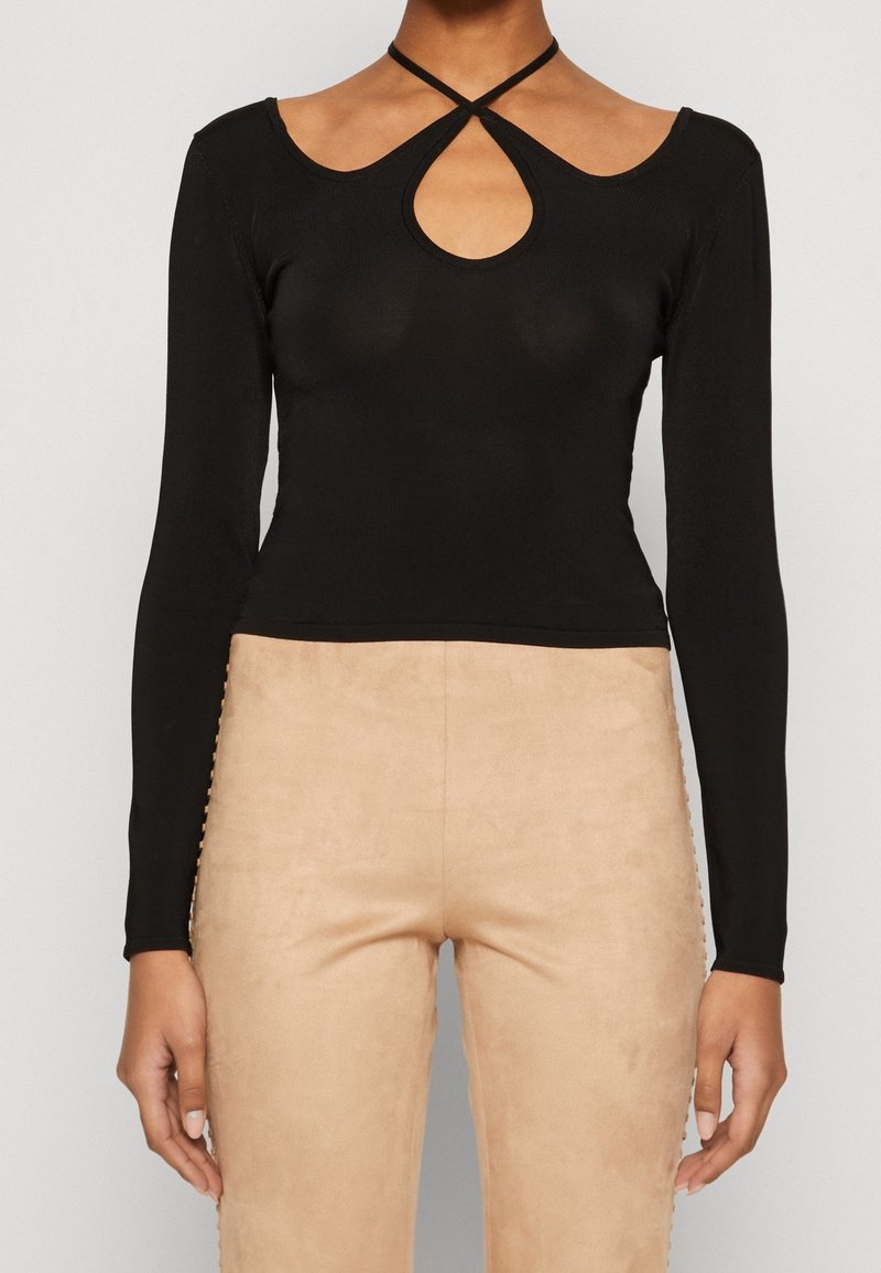 T-shirt noir à manches longues avec un décolleté en forme de trou de serrure et un tissu texturé. Accompagné d'un pantalon ajusté en suédine beige.