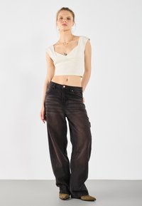 Hvid cropped top med korte ærmer, parret med løse sorte denimbukser med en falmet tekstur og knapdetaljer. Brune spidse sko.