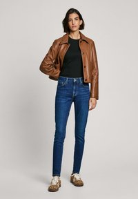 Hnedá kožená bunda, čierne tričko, modré úzke džínsy a vzorované tenisky. Hladká textúra, priliehavý strih a kontrastné farby.