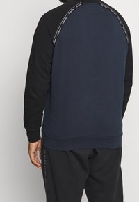 Sudadera azul marino con mangas negras, con un detalle de logotipo a lo largo de la costura del hombro, dobladillo y puños acanalados, confeccionada en tela suave.
