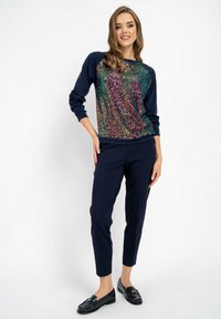 Granatowy sweter z kolorowym wzorem z cekinów z przodu, zestawiony z granatowymi spodniami i czarnymi loafersami, o dopasowanej sylwetce.