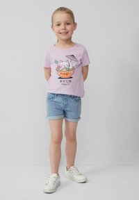 Lila kortekleding t-shirt met een cartoonkat in een noedelkom met eetstokjes, gecombineerd met opgerolde denimshorts en witte sneakers.