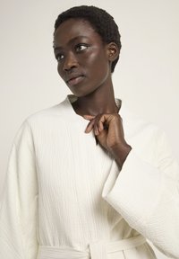 White textured robe with a shawl collar, long sleeves, and a waist belt, featuring a quilted pattern and a soft, plush material.