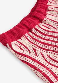 Häkeltextil mit abwechselnden Mustern in Rot und Creme, umrandet von einem strukturierten Rand. Weiches, flexibles Material mit wellenförmigem Design.