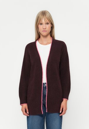 Burgunderfarget cardigan med strukturstrikk, med en rosa kant langs den åpne fronten og ermekantene. Båret over en hvit skjorte og denim.