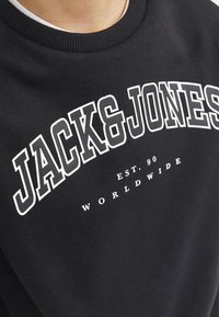 Czarna bluza z białym napisem graficznym "JACK & JONES" łukowato umieszczonym na klatce piersiowej, z mniejszymi napisami "EST. 90" i "WORLDWIDE" poniżej.