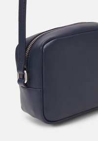 Borsa a tracolla in pelle blu navy con forma rettangolare, zip in argento, tracolla sottile e superficie liscia. Dettagli di cucitura evidenti lungo i bordi.