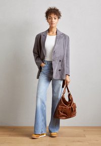Gray suede double-breasted blazer, white fitted shirt, flared light blue jeans, yellow platform shoes, and brown leather handbag with pockets.