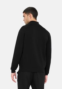 Felpa nera a maniche lunghe con colletto alto, tessuto testurizzato e polsini a coste. Presenta un design senza cuciture e una vestibilità comoda.