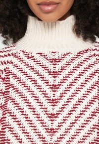 Κόκκινο και κρεμ πλεκτό πουλόβερ με ψηλό ριμπ λαιμόκοψη και σχέδιο σε σχήμα βέλο�υς. Διαθέτει υφή νήματος και εφαρμοστή γραμμή.