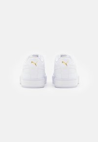 Fehér sneaker sima bőr felülettel, aranyszínű logóval, párnázott gallérral és vastag gumitalppal. Jellemzője a minimalista design és textúra.