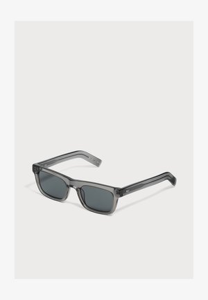 Lunettes de soleil rectangulaires gris foncé avec des montures épaisses translucides et des verres foncés sur fond blanc.