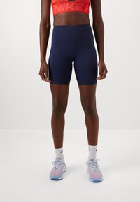Marineblå høyt livs athletic shorts med side lommer, laget av elastisk stoff. Kombinert med lyse løpesko og hvite sokker.