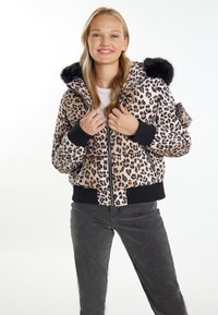 Giacca bomber con stampa leopardata e cappuccio in finta pelliccia nera, chiusura con zip, tasche laterali e polsini a costine. Abbinata a pantaloni grigi scuri.