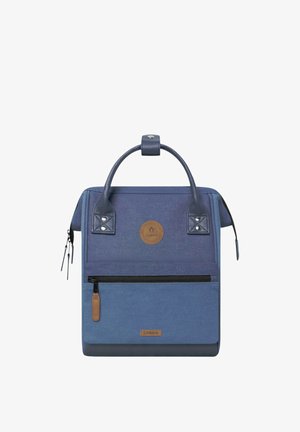 Quadratischer dunkelblauer Rucksack mit zwei Tragegriffen, vorderer Reißverschlusstasche und braunen Logo-Patches mit der Aufschrift "CABAIA" auf Stoff und Leder.