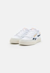 Sneaker bianche con una suola testurizzata di colore crema. Presenta accenti blu e arancione, una tomaia forata e chiusura con lacci.