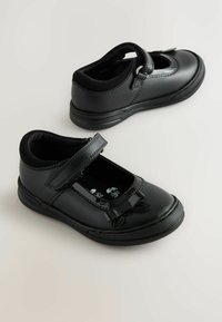 Schwarze Mary-Jane-Schuhe mit lackierter Zehenkappe, verstellbarem Riemen und Schleifenakzent. Hergestellt aus glattem synthetischem Material mit strukturierten Gummisohlen.