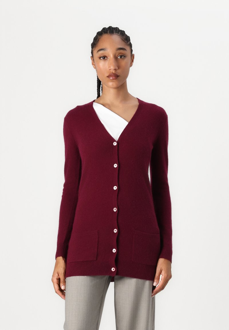 Burgunderfarbener Cardigan aus weichem Strickstoff, mit V-Ausschnitt, langen Ärmeln, zwei vorderen Taschen und weißen Knöpfen vorne.