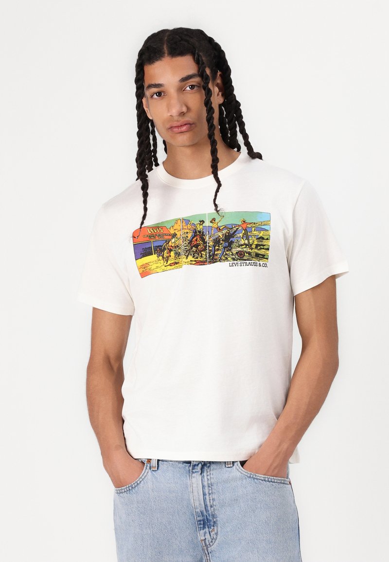 Cremefarbiges Baumwoll-T-Shirt mit einem bunten Grafikdruck, der Szenen und Text zeigt. Kurze Ärmel, Rundhalsausschnitt, lässige Passform. Jeans aus Denim.