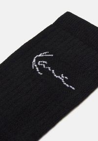 Fekete kötött zokni, fehér hímzett mintával, amely egy kezet ábrázol. Az egész zokni texturált bordás mintázatú. Standard zokni forma.