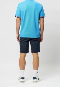 Jasnoniebieska koszulka polo z kontrastowymi czarno-białymi ściągaczami, zestawiona z ciemnogranatowymi szortami. Uzupełniona białymi skarpetkami do kostek i sneakersami.