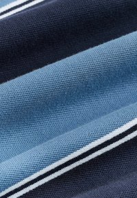 Közelkép egy texturált anyagról, amely diagonális tengerészkék és világoskék csíkokkal rendelkezik, vékony fehér és fekete vonalakkal kiemelve.