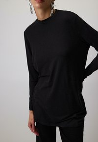 Čierny top s dlhým rukávom, vysokým golierom a úzkym strihom, vyrobený z hladkej látky. Obsahuje rovný lem a minimalistický dizajn.