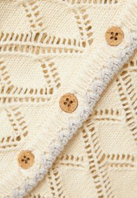 Cardigan lavorato a maglia color crema con un motivo a diamante texture, dotato di bottoni in legno e di un bordo a coste a contrasto lungo i lati.