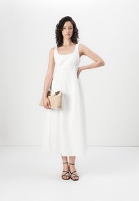 Vit, ärmlös maxiklänning med fyrkantig halsringning och rynkad midja. Tillsammans med en strukturerad guldig clutch och svarta sandaler med remmar.