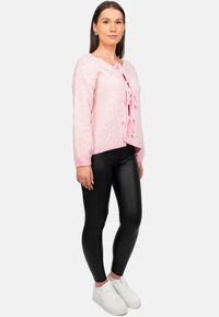 Maglione in rosa pallido lavorato a maglia con motivo leopardato e chiusura a fiocco. Abbinato a leggings in finta pelle neri e sneakers bianche.