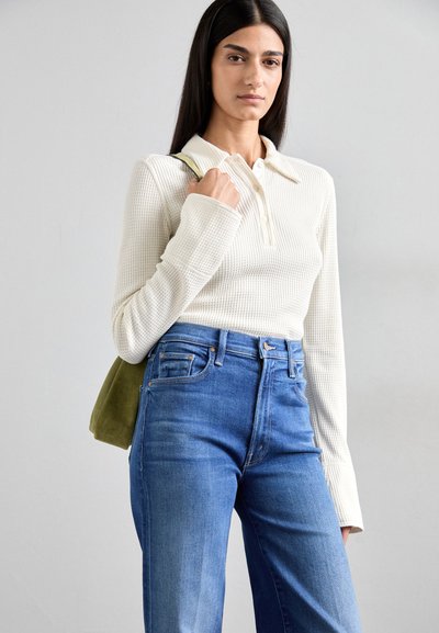 Cream-colored, ribbed long-sleeve top with a collared neckline and button placket paired with high-waisted blue jeans and a green bag.