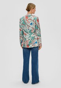 Farbiger Blazer mit Paisleymuster in Türkis, akzentuiert mit Rot, Weiß und Blau, kombiniert mit weit geschnittenen Denim-Hosen.