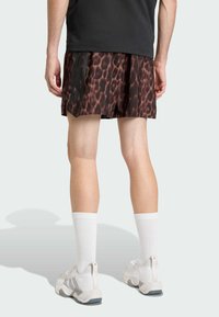 Musta t-paita, ruskeat leopardikuvioiset pliseeratut shortsit, valkoiset sukat ja harmaat urheilukengät. Shortseissa on pystysuorat mustat raidat sivuilla.