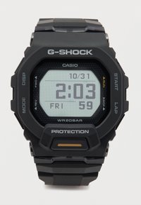 Reloj digital G-Shock con correa de goma negra, caja rectangular y display LCD gris, con un patrón hexagonal y marcas blancas.