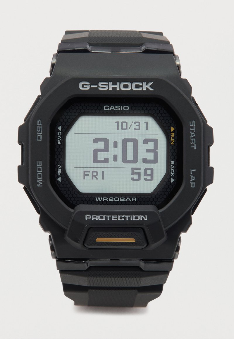 Reloj digital G-Shock con correa de goma negra, caja rectangular y display LCD gris, con un patrón hexagonal y marcas blancas.