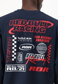 Camiseta de manga larga de color navy con un atrevido texto gráfico en rojo y blanco y logotipos, incluyendo "Red Bull Racing" y varios diseños temáticos de automovilismo.